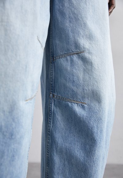 Ανοιχτό μπλε τζιν παντελόνι με χαλαρή εφαρμογή, που διαθέτει ορατές ραφές, πολλαπλές τσέπες και ελαφρώς ξέφτιασμα υφή.