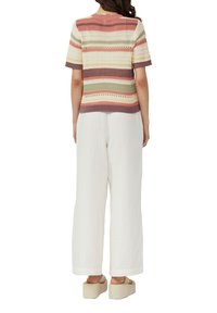Gestreiftes Stricktop in Rosa, Grün und Creme mit kurzen Ärmeln; kombiniert mit weißen, weit geschnittenen Hosen und beigen Plateausandalen.
