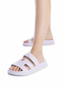 Chanclas de goma de color lila claro con diseño de punta abierta, que cuentan con dos correas anchas y detalles recortados en los lados. Textura suave.