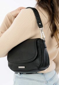 Czarna skórzana torebka na ramię o fakturowanej powierzchni, zaokrąglonym kształcie, z klapkowym zamknięciem i plecionym paskiem ze srebrnymi metalowymi okuciami.