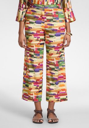 Pantalones de corte ancho recortados con un patrón rectangular abstracto multicolor, combinados con un top a juego, sandalias marrones y una pulsera dorada.