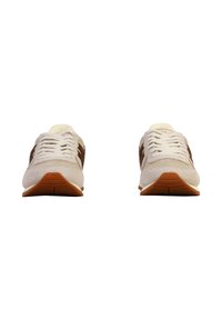Beige mockasin sneakers med bruna accenter, vita snören och gummisulor. Frontal vy som visar en rundad tå och textilmaterial.