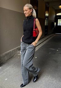 Musta ilmanhiha toppi, jossa on korkea kaula-aukko, harmaat raidalliset leveälahkeiset housut ja mustat kärkitossut. Pieni punainen käsilaukku täydentää asun.