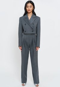 Szary, dwurzędowy marynarka o teksturowanym wykończeniu i szerokich klapach, zestawiona z spodniami o wysokim stanie i plisach w dopasowanym odcieniu.