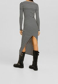 Vestito a righe bianche e nere con maniche lunghe, spacchi alti su un lato, abbinato a stivali neri fino al ginocchio con fibbie.