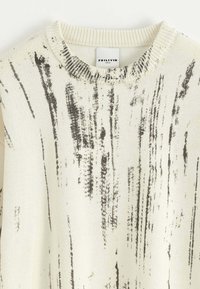 Pull crème avec des rayures abstraites noires, col rond, col côtelé et texture en maille fine. L'étiquette indique "FRILIVIN."