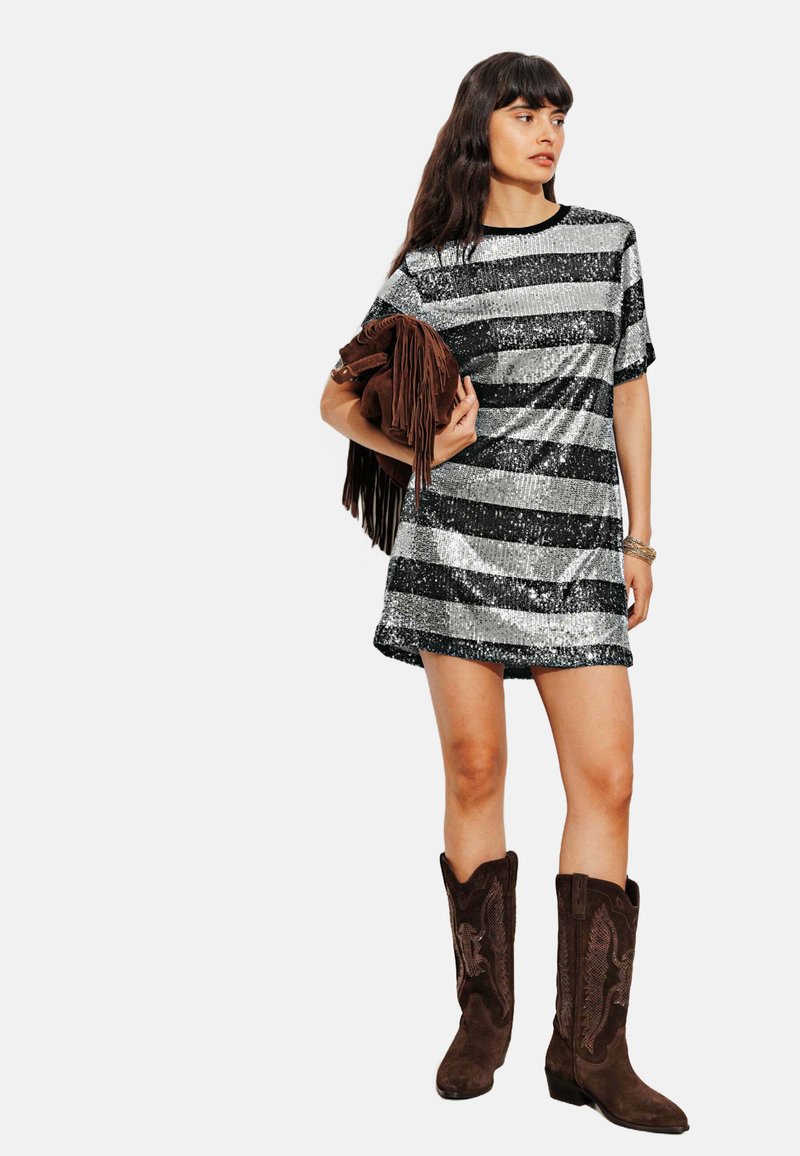 Robe mini en sequins argentés et noir avec des manches courtes, associée à des bottes de cowboy en suède marron, et tenant un sac à main frangé marron.