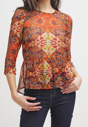Blouse colorée et à motifs avec une coupe péplum, dotée d'un col rond et de manches trois-quarts. Le matériau semble léger et semi-transparent.
