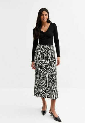 Lange zwart-witte zebra print rok gecombineerd met een aansluitend zwart langmouwtop, wat een slanke silhouet creëert. Zwarte puntige schoenen maken de look compleet.
