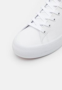 Hvite sneakers med en glatt syntetisk overdel, rund tå, flate lisser og en teksturert gummisåle med fiskebensmønster.