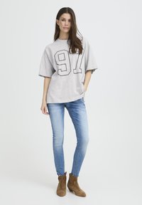 Pelēka oversized T-krekls ar melnu "97" grafiku, kombinēts ar piegulošām gaiši zilām džinsām un brūnām zamšādas potīšu zābaciņām. Vienkāršs, ikdienišķs stils.