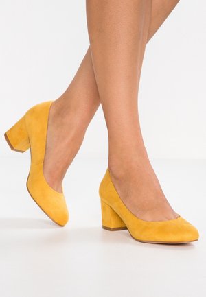 Gule ruskinds stilethæle med rund tå og blokhælsdesign. Teksturen er glat og blød, med en solid hæl til støtte.