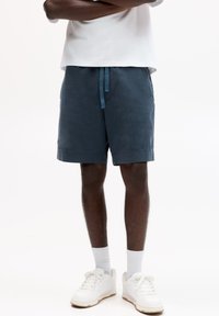 Marineblaue Shorts mit einem Kordelzug und elastischem Bund, aus leichtem Stoff gefertigt. Kombiniert mit weißen Turnschuhen und Socken.