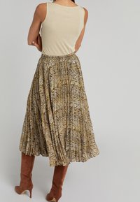 Plissé midi-jurk in bruin en crèmekleurige slangprintstof, gecombineerd met een lichtbeige tanktop. Bruine thigh-high hakschoenen maken de look af.