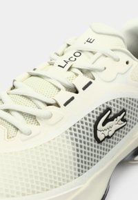 Lacoste sporta kurpes gaiši pelēkā acs audumā ar gumijas zoli, ar baltām šņorēm un melnu krokodila logo sānos.