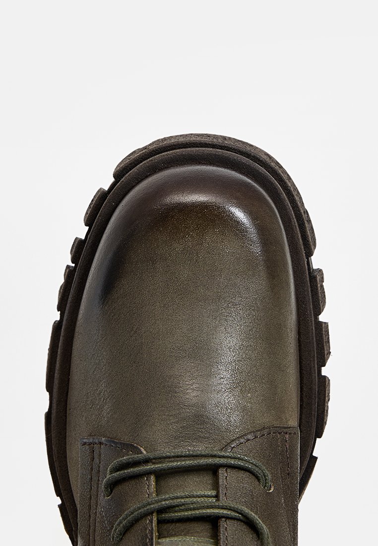 Botte de cheville en cuir vert avec un bout rond, tige texturée, semelle noire épaisse et lacets verts. Fini lisse avec une légère brillance.