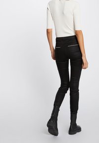 Jeans ajustados negros de cintura alta, con dos bolsillos traseros con costuras en contraste, combinados con botas negras de tobillo y una camiseta blanca.