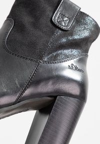 Zwarte enkellaars met hak, uitgevoerd in een combinatie van glad en getextureerd leer. Voorzien van een decoratieve band met een gestikte detail en logo.