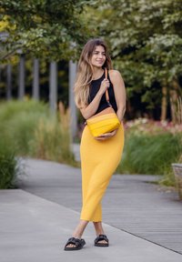 Žlutá texturovaná maxi sukně, černý top bez rukávů a černé ploché sandály. Krosová taška se žlutým tělem a hnědým horním akcentem.