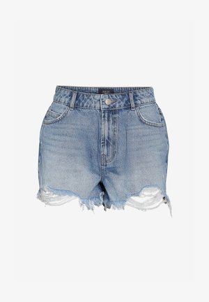 Kvinne stående iført en knallrød kortermet skjorte, blå slitte denimshorts og brune joggesko, poserer med én hånd i lommen.