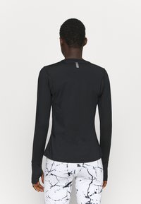 Svart långärmad sporttröja med rund halsringning och tumhål, med subtila vita detaljer på baksidan. Matchad med vita marmorerade leggings.