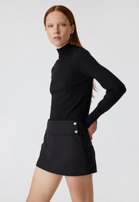 Maglione aderente nero a collo alto in maglia testurizzata abbinato a una mini gonna nera a vita alta con due bottoni argentati decorativi.
