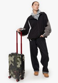 Kufr velikosti kabiny v zeleném maskáčovém vzoru s černými doplňky, červenou rukojetí a kolečky. Stylový a odolný design s tvrdou skořepinou.