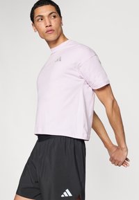 Hele roosa lühike t-särk lühikeste varrukatega ja hallide logode detailidega, mida on kombineeritud mustade spordipükstega, millel on valge logo ja elastne vöökoht.