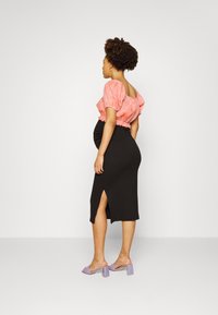 Top cropped texturizado rosa, saia bodycon preta com fenda lateral e sandálias de bloco de calcanhar lavanda. Modelo mostrando um perfil lateral.