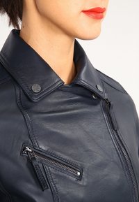 Námorně modrá kožená bunda s širokým l ímcem, zipovou kapsou a drukovými akcenty s hladkou texturou.