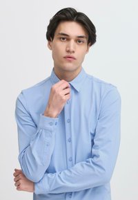 Lichtblauwe langwerpige blouse met een button-down kraag, voorzien van bijpassende knopen en een gladde, zachte textuur.