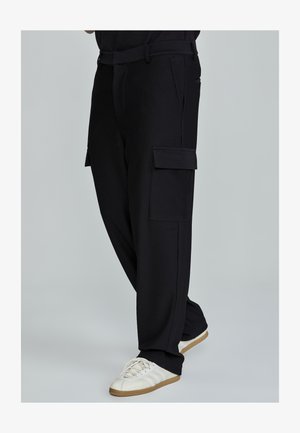 Černé žebrované cargo kalhoty s volným střihem, obsahující dvě boční kapsy a strukturovanou látku; stylizované s bílými teniskami.