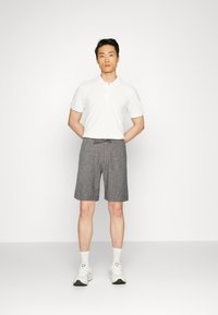 Hvit poloskjorte med korte ermer, kombinert med grå rutete shorts. Modellen har på seg hvite sneakers med lysegrå detaljer og ankelsokker.
