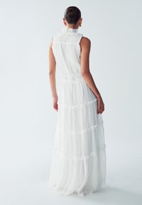 Abito maxi bianco con colletti arricciati, tessuto trasparente e testurizzato, strati sovrapposti e sottili motivi a pois. Design con schiena scoperta.