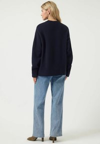 Marineblauw oversized sweater met een ronde hals, gecombineerd met lichtblauwe high-waisted jeans en bruine haklaarzen. Zachte textuur en comfortabele pasvorm.
