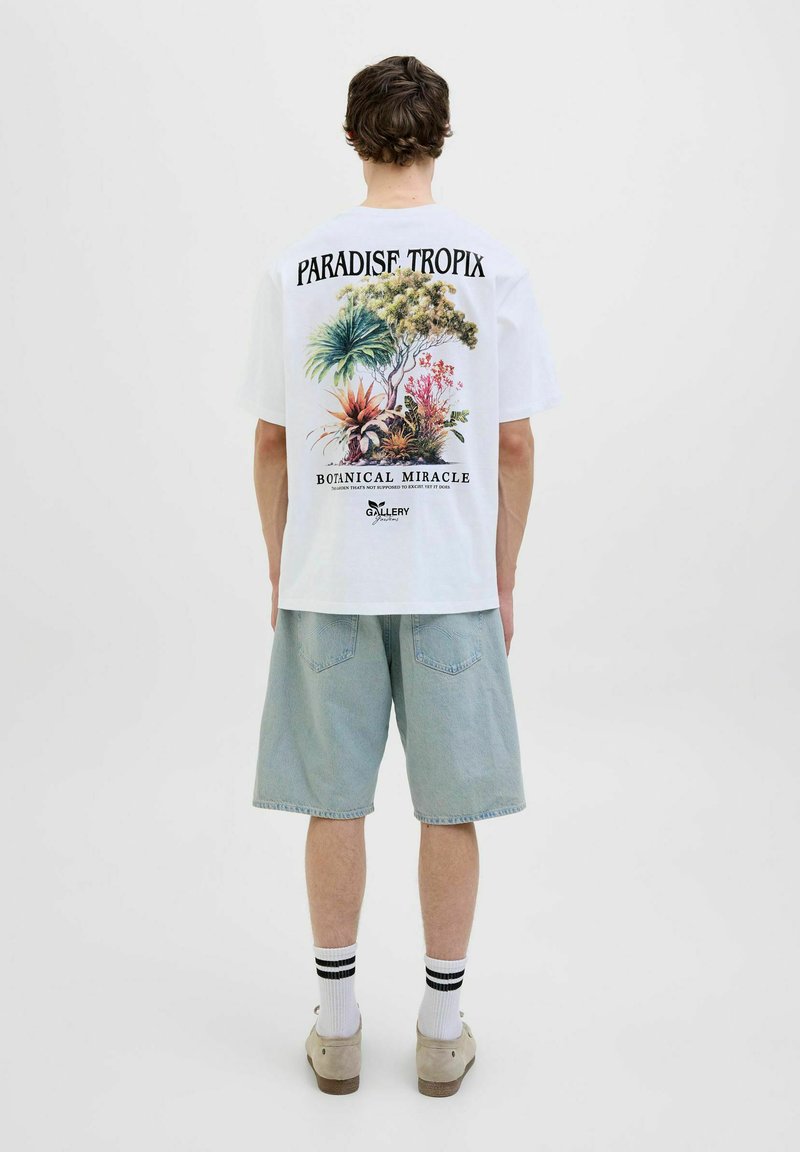 Hvid kortærmet T-shirt med et botanisk print på ryggen, teksten "PARADISE TROPIX" og "BOTANICAL MIRACLE", parret med lyseblå denimshorts.