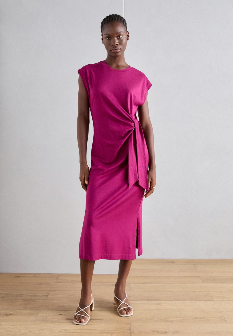 Fuchsia knielanges Kleid aus weichem Stoff mit kurzen Ärmeln, gedrehtem Frontdetail, seitlichem Schlitz und lockerem Sitz. Getragen mit Riemchen-Heels.
