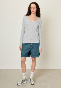 Pelēks garām piedurknēm krekls ar apaļu kakla izgriezumu, kombinēts ar zilām džinsa šortiem līdz ceļiem. Modelis valkā pelēkas sporta kurpes un baltas zeķes.