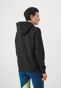 Čierna mikina s kapucňou, dlhými rukávmi a voľným strihom, s jemnou textúrou a ribbed manžetami, zobrazená zozadu.