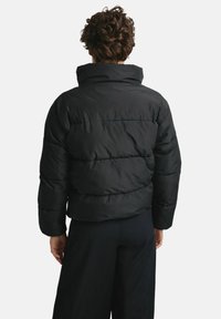 Czarna puchowa kurtka z wysokim kołnierzem, prążkowanymi mankietami i poziomym przeszyciem. Posiada pudełkowaty krój i miękki, teksturowany materiał.
