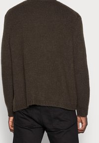 Maglione marrone lavorato a maglia con un design a coste. Vestibilità leggermente ampia, caratterizzato da un collo a giro e un orlo posteriore allungato.