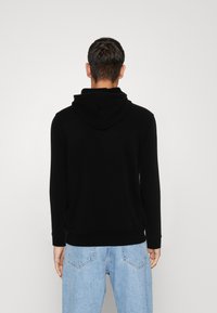 Felpa nera con cappuccio dal tessuto morbido, maniche lunghe e vestibilità rilassata. Abbinata a jeans in denim chiaro, di taglio ampio.