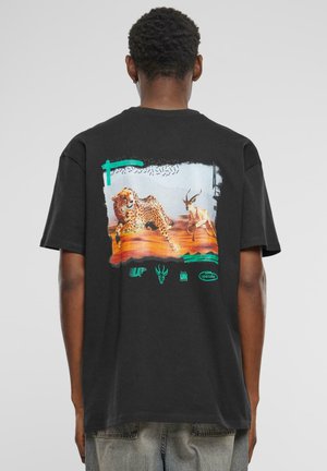 Sort bomuld t-shirt med et farverigt grafik af en leopard og en gaselle, med grønne akcentelementer og logoer på den nederste del.