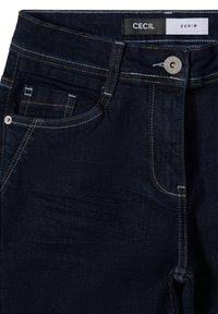 Vaqueros de mezclilla azul oscuro con costuras amarillas, que presentan un bolsillo delantero, cierre de botón y una etiqueta con la inscripción "CECI L DENIM" en la cinturilla.