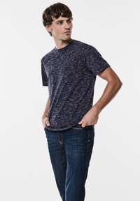 Mörkblå kortärmad t-shirt med en texturerad, prickig mönstring, i kombination med mörka denimjeans. Avslappnad passform och rundad halsringning.