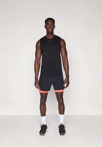 Juoda be rankovių sportinė palaidinė derinama su juodais šortais su oranžine akcentine juosta. Modelis vilki juodus sportinius batelius ir baltas kojines.