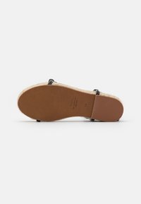 Espadrilkové sandály s jutu, černými popruhy a hnědým koženým dnem. Mají strukturovaný povrch a minimální branding.