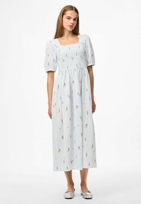 Gai zils maxi kleita ar īsām puff piedurknēm, kvadrātveida dekoltē, smockotu korseti un ziedu izšuvumiem. Sudrabaini apavi noslēdz izskatu.