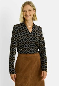 Chemisier à manches longues en noir avec un motif géométrique de vagues en argent et or. Il présente un devant à boutons et un col.