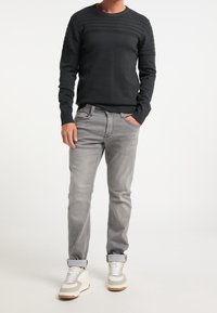 Dunkelgrauer Strickpullover mit strukturierten horizontalen Streifen, kombiniert mit hellgrauen Jeans und weißen Sneakers mit grauen Akzenten. Lässige Passform.